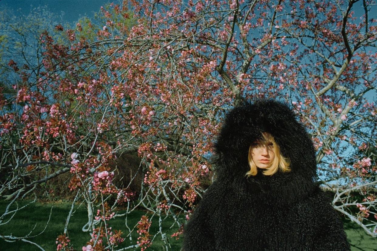 a woman in a black hooded coat standing in front of a flowering tree