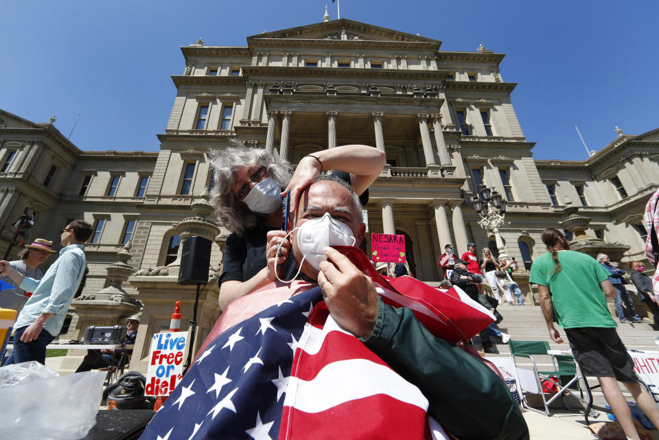 Annette Rafacz gives Manny Orovcoa a free haircut at the State Capitol during a rally in Lansing, Mich., Wednesday, May 20, 2020. Barbers and hair stylists are protesting the state's stay-at-home orders, a defiant demonstration that reflects how salons have become a symbol for small businesses that are eager to reopen two months after the COVID-19 pandemic began. (AP Photo/Paul Sancya)