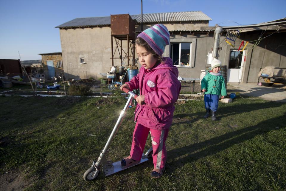 In this photo taken Thursday March 27, 2014 Crimea's Tatar Sedomed Setumerov's children, Diana, 4, left, and Enver, play in the yard of their recent squatter settlement in Lozovoye-2 not far from Simferopol, Crimea. On Saturday the Crimean Tatar Qurultay, a religious congress will determine whether the Tatars will accept Russian citizenship and the political system that comes with it, or remain Ukrainian citizens on Russian soil. (AP Photo/Pavel Golovkin)