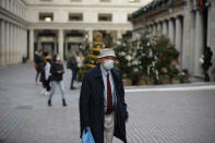 A man wearing a face mask walks backdropped by Christmas trees in Covent Garden, during England's second coronavirus lockdown in London, Thursday, Nov. 26, 2020. As Christmas approaches, most people in England will continue to face tight restrictions on socializing and business after a nationwide lockdown ends next week, the government announced Thursday. (AP Photo/Matt Dunham)