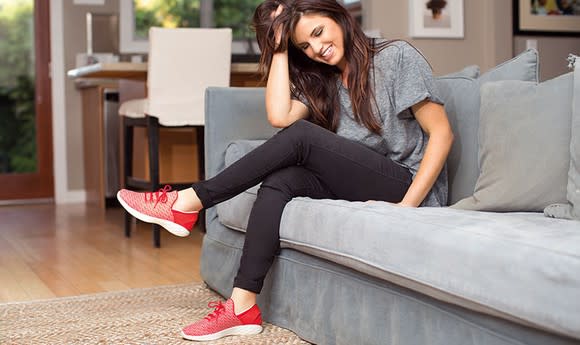 A young woman sitting on a couch wearing workout clothes and a red pair of Skechers shoes.