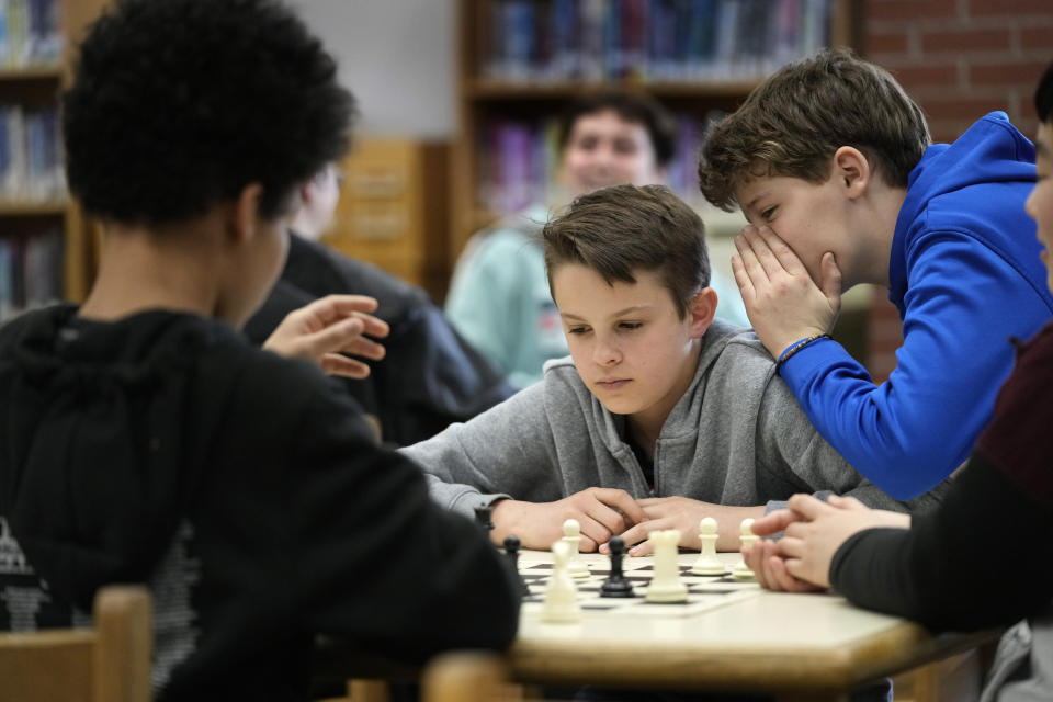 Owen Isenhour whispers advice to Eli Marquis during a Reeds Brook Middle School after-school chess practice, Tuesday, April 25, 2023, in Hampden, Maine. Part-time chess coach and full-time custodian David Bishop led his elementary and middle school teams to state championship titles this year. (AP Photo/Robert F. Bukaty)