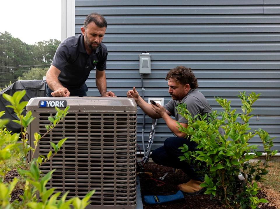 Nihat Yucel and Andrew Ayers of Klimatology HVAC work on an air conditioning unit outside a residence in Raleigh, North Carolina, on Tuesday, Aug. 15, 2023. Experts say AC systems can cool a home to 20 to 30 degrees less than the outdoor temperature.