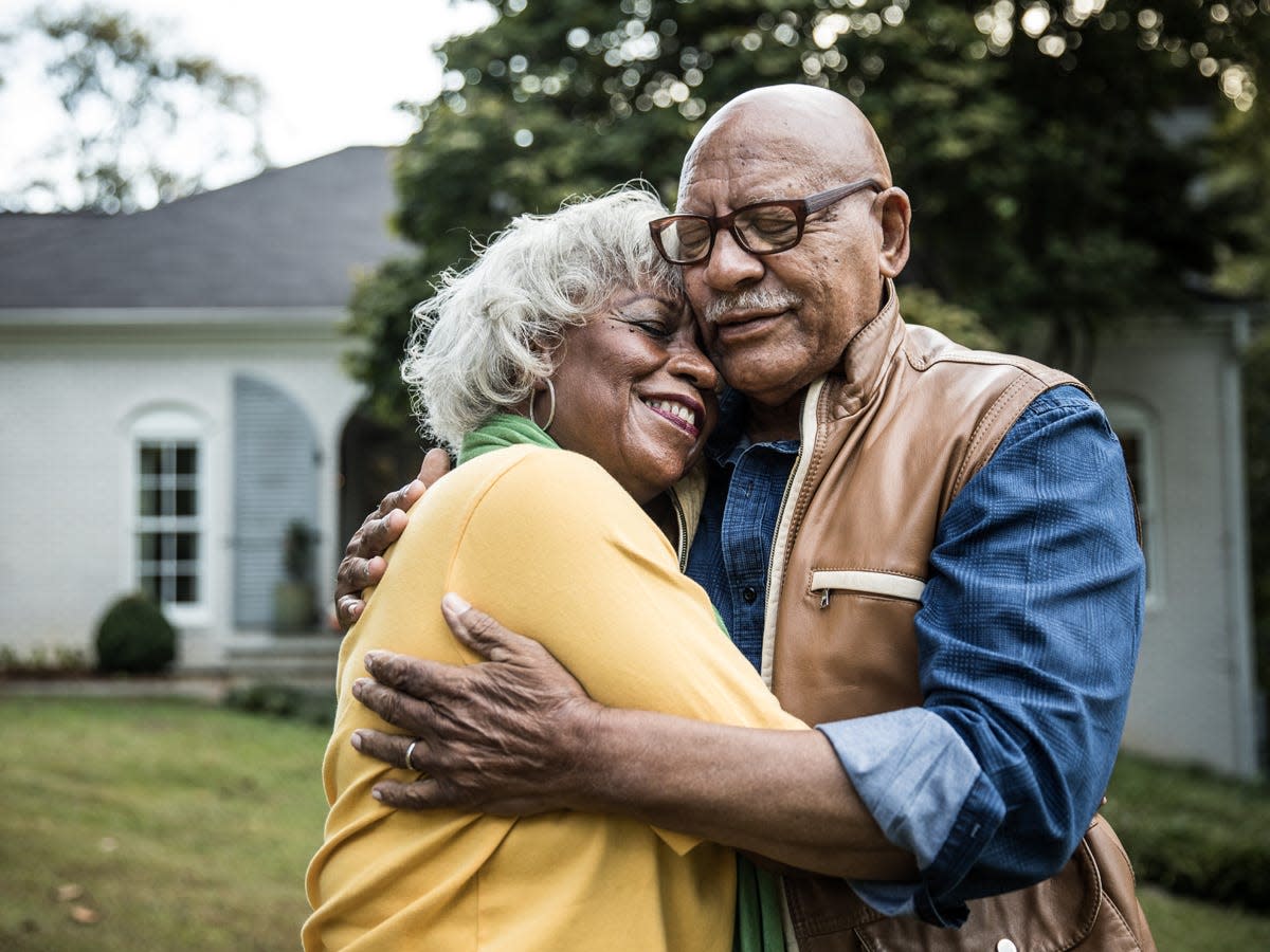 Senior couple embracing and smiling in front of a house.