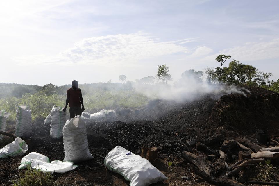 Deo Ssenyimba stands near a heap of burning charcoal in Gulu, Uganda, May 27, 2023. The burning of charcoal is now restricted business across northern Uganda amid a wave of resentment by locals who have warned of the threat of climate change stemming from the uncontrolled felling of trees by outsiders. "We are not going to stop," Ssenyimba said, who has been active in northern Uganda for 12 years. (AP Photo/Hajarah Nalwadda)