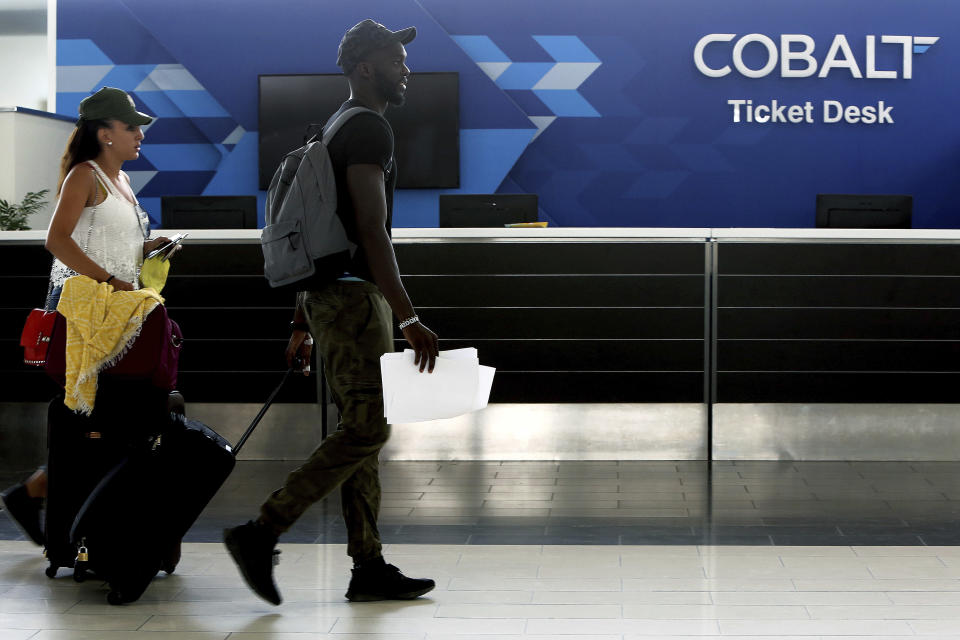 Passengers walk in front of Cobalt air ticket office at Larnaca international airport, Cyprus, Thursday, Oct. 18, 2018. Cyprus-based airline Cobalt Air says Thursday it has indefinitely suspended all of its operations amid a struggle to find investors. (AP Photo/Petros Karadjias)