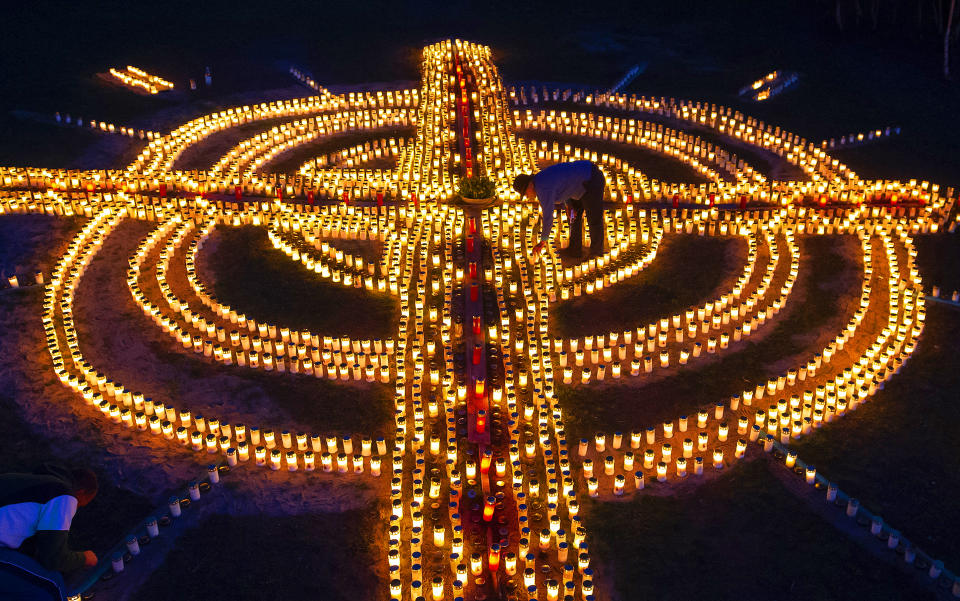 Tax advisor and Catholic Gertrud Schop, right, lights candles forming a giant cross in memory of coronavirus victims in Germany in Zella-Mehlis, central Germany, Friday, April 17, 2020. Schop and volunteers lit close to 4000 candles which took seven hours to complete. (AP Photo/Jens Meyer)