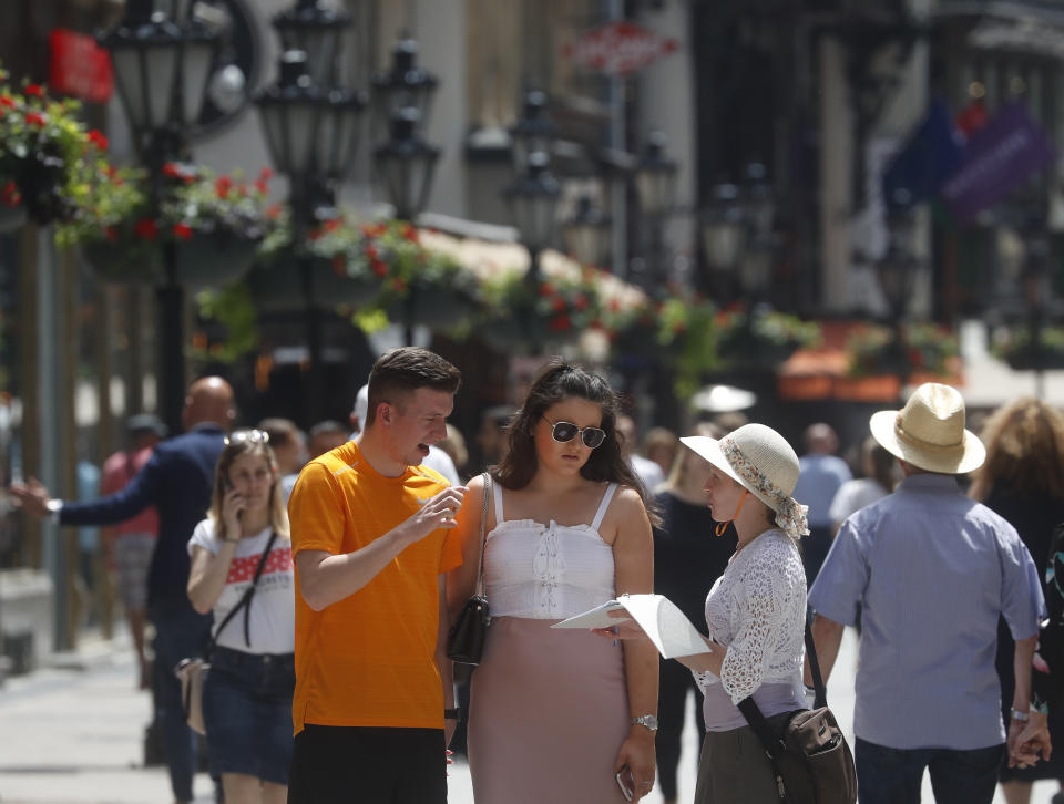 In this photo taken on Wednesday, June 5, 2019, tourists talk with a woman offering tourism services on Vaci Street in downtown Budapest, Hungary. A tourism boom in the Hungarian capital has led to major congestion on the river flowing through the city, with sightseeing boats and floating hotels competing for better positions in front of spectacular neo-Gothic buildings, ornate bridges and churches lining the Danube.(AP Photo/Laszlo Balogh)