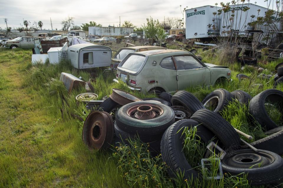 Cars, tires and other items scattered on a grassy field.