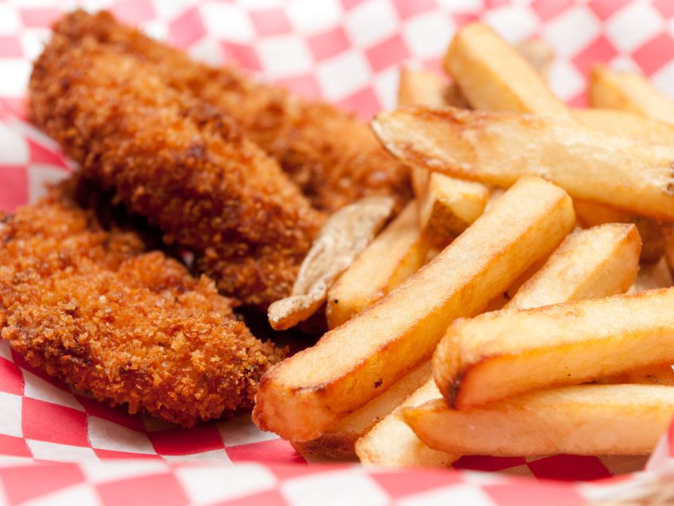 basket of three chicken tenders and a side of fries served on red checkered paper