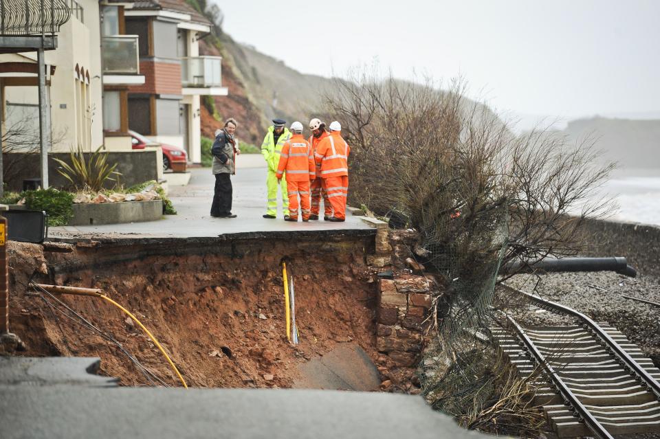 Workmen assess a huge hole exposing ground services and exposed railway track after the sea wall collapsed in Dawlish, England, Wednesday, Feb. 5, 2014. Heavy rain, high tides and strong winds pounded England’s southern coast Wednesday, washing away a stretch of rail line, damaging an iconic seaside pier and leaving thousands of homes without power. (AP Photo/PA, Ben Birchall) UNITED KINGDOM OUT, NO SALES, NO ARCHIVE