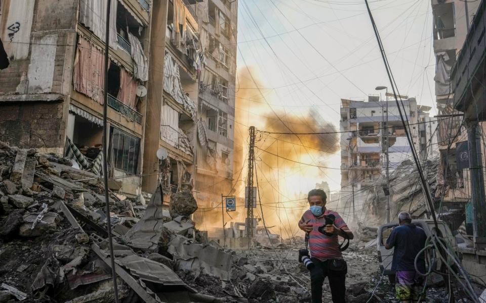 A photographer runs for cover as a smoke raises in the background following an Israeli airstrike in Dahieh, Beirut, Oct 4