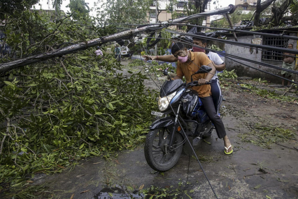 Motorists make their way through damaged cables and a tree branch fallen in the middle of a road after Cyclone Amphan hit the region in Kolkata, India, Thursday, May 21, 2020. People forgot about social distancing and crammed themselves into government shelters, minutes before Cyclone Amphan crashed in West Bengal. The cyclone killed dozens of people and the coronavirus nine in this region, one of India’s poorer states. Even before the cyclone, its pandemic response was lagging; the state has one of the highest fatality rates from COVID-19 in India. With an economy crippled by India’s eight-week lockdown, and health care systems sapped by the virus, authorities must tackle both COVID-19 and the cyclone’s aftermath.(AP Photo/Bikas Das)