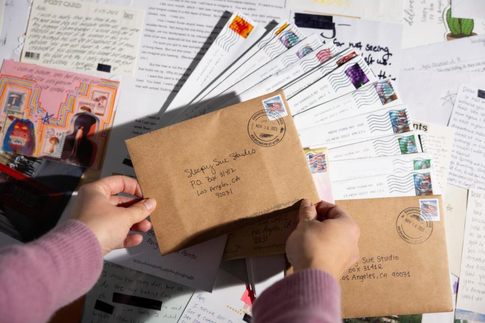 A person holds an envelope, with a collection of envelopes in the background.