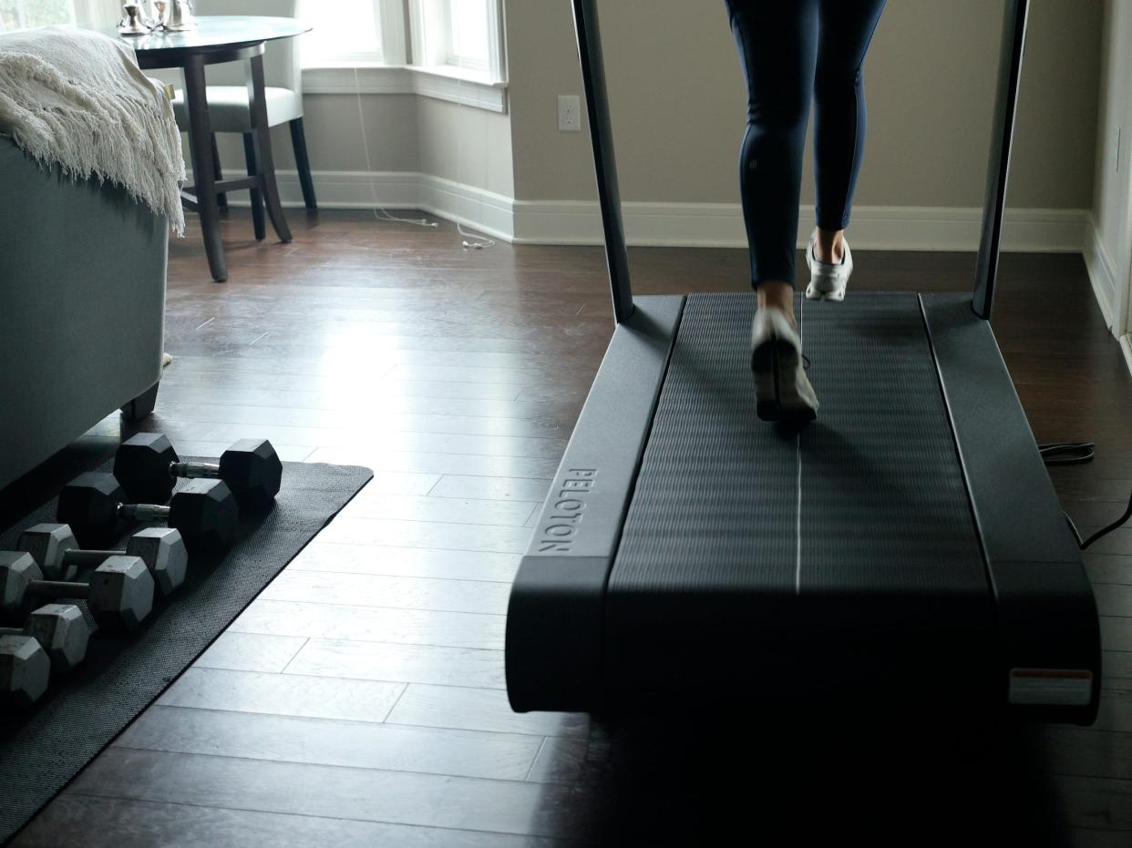 Woman runs on Peloton Tread treadmill in living room next to free weights