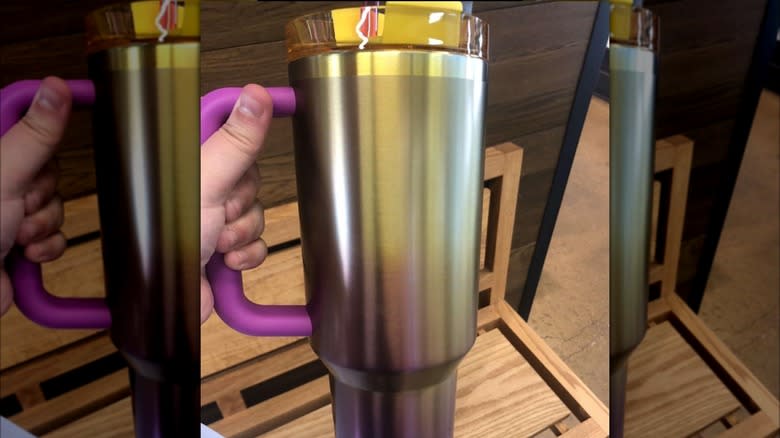 A hand holding the unreleased gold and pink Starbucks x Stanley May tumbler