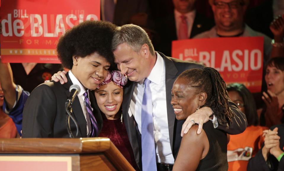 FILE - In this Sept. 10, 2013 file photo, New York Democratic mayoral hopeful Bill de Blasio embraces his son Dante, left, daughter Chiara, second from left, and wife Chirlane McCray, right, at his election headquarters after polls closed in the city's primary election in New York. Dante, 16, whose large, perfectly coiffed afro is hard to miss at campaign stops and in a TV spot as dad runs for New York City mayor. The dress code at his public high school in Brooklyn includes does not have a hair restriction. (AP Photo/Kathy Willens, File)