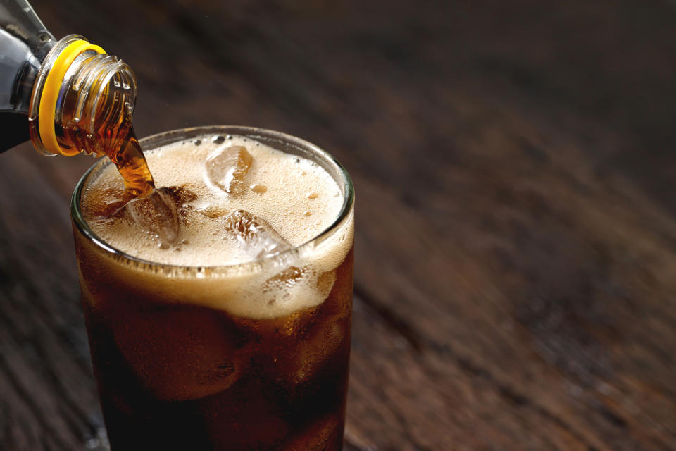 Pouring a bubbly soft drink into a glass with ice cubes, close-up view, illustrating a beverage-related article