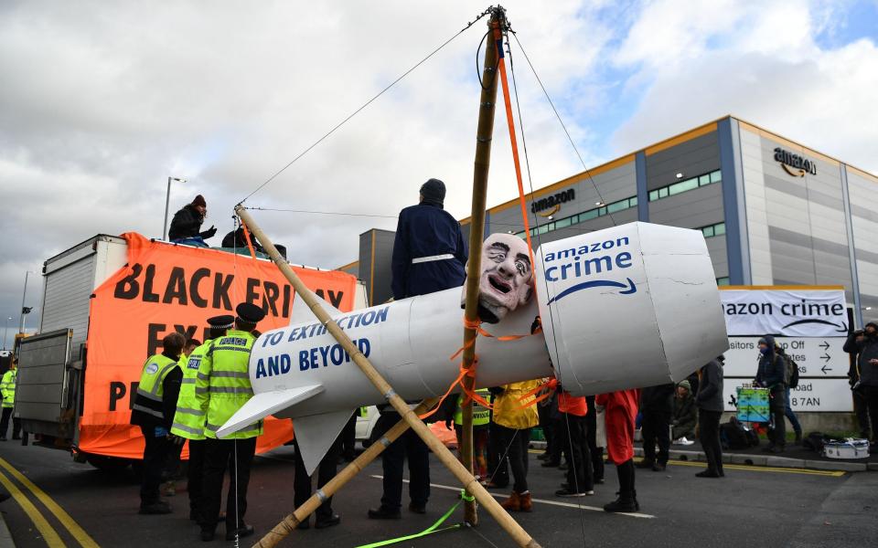 An activist from the Extinction Rebellion (XR) climate change group sits on a giant wooden rocket as they block the exit to an Amazon distribution centre in Tilbury - BEN STANSALL/AFP via Getty Images