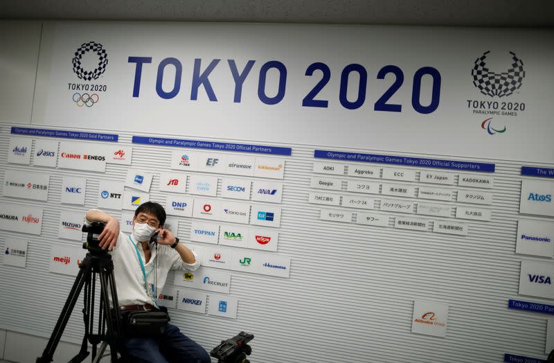 Un camarógrafo con una máscara facial protectora, frente a un cartel que muestra los logos de los Juegos Olímpicos y Paralímpicos de Tokio 2020, en el lugar de conferencia de prensa.