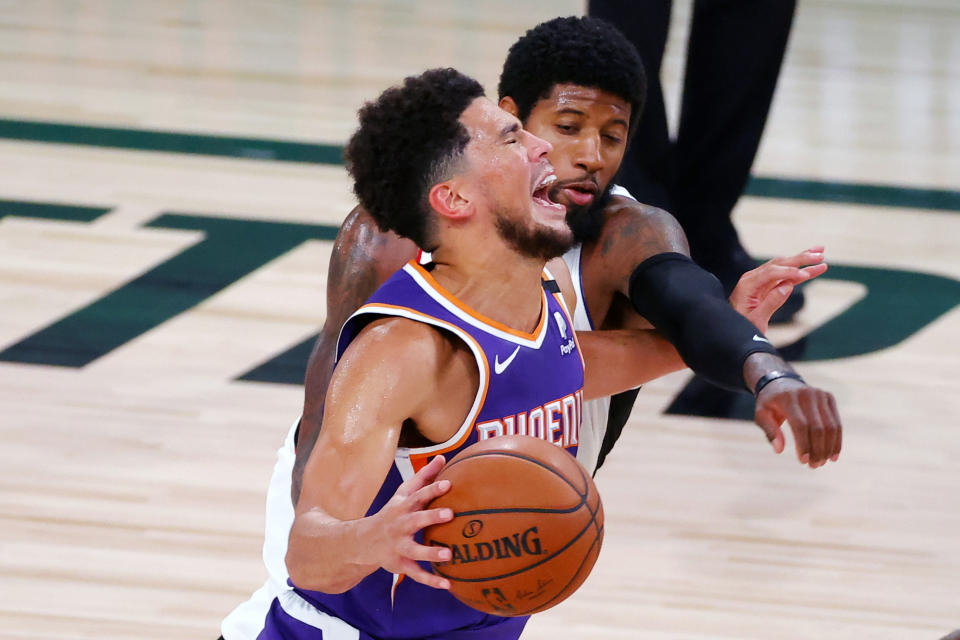 Phoenix Suns' Devin Booker draws a foul from Los Angeles Clippers' Paul George, rear, during an NBA basketball game Tuesday, Aug. 4, 2020, in Lake Buena Vista, Fla. (Kevin C. Cox/Pool Photo via AP)