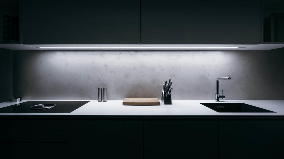 A dark kitchen with overhead counter lights illuminated