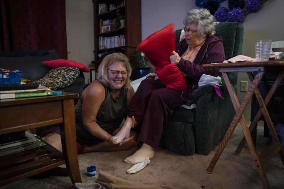 Susan Ryder, 54, giggles as she applies an ointment to the base of her mother's foot before bedtime, Monday, Nov. 29, 2021, in Rotterdam Junction, N.Y. When Ryder was laid off about a month after taking her mother out of the nursing home, she embraced it as a chance to fully devote herself to caregiving. (AP Photo/Wong Maye-E)