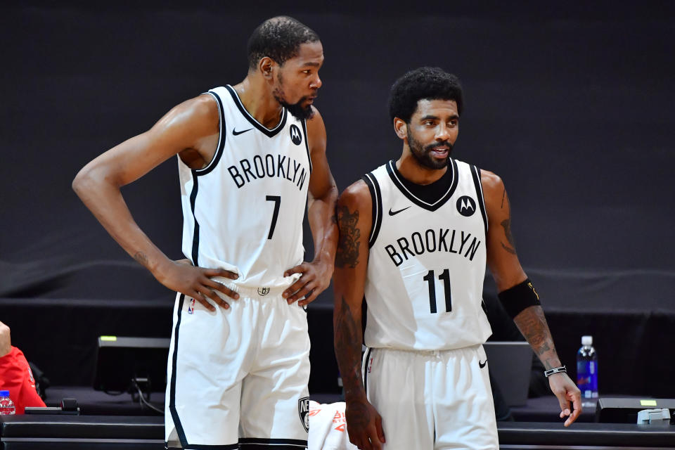 Kevin Durant and Kyrie Irving talk near the scorers table during a game.