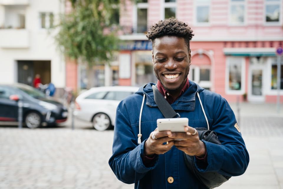 Smiling young man looks at his cell phone with a colorful city street behind him