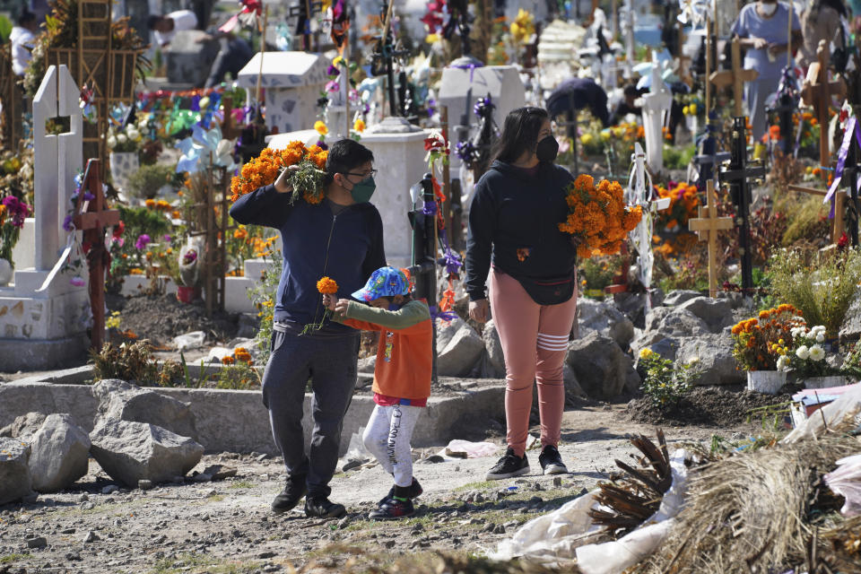 A family brings flowers to the Valle de Chalco municipal cemetery as people begin to arrive to pay their respects to their dead, on the outskirts of Mexico City, Sunday, Oct. 31. 2021. (AP Photo/Marco Ugarte)