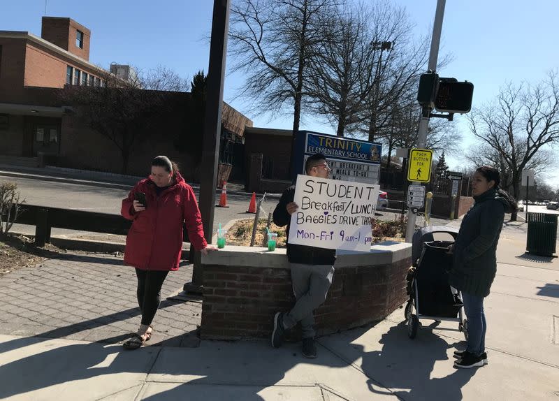 FILE PHOTO: Mario Bravo, a school safety aide at Trinity Elementary School, holds a sign about free bagged meals for schoolchildren, in New Rochelle