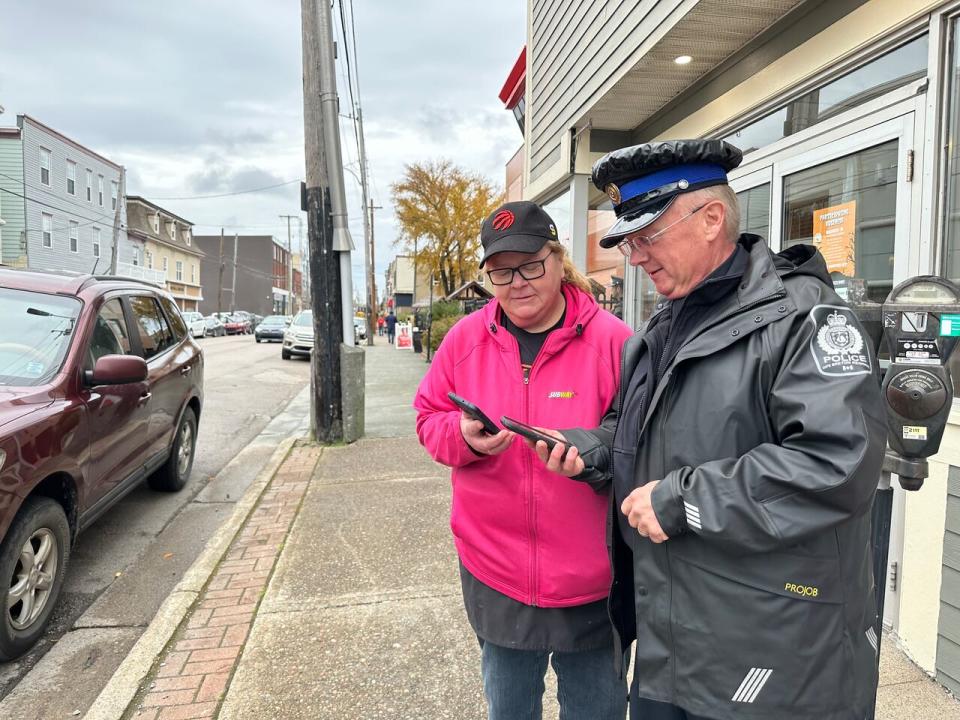 Subway area manager Teresa Rowe and Cape Breton Regional Police Officer Gary Fraser use a mobile phone app to communicate with other members of the Downtown Sydney Business Watch Group.  (Holly Connors/CBC - image credit)