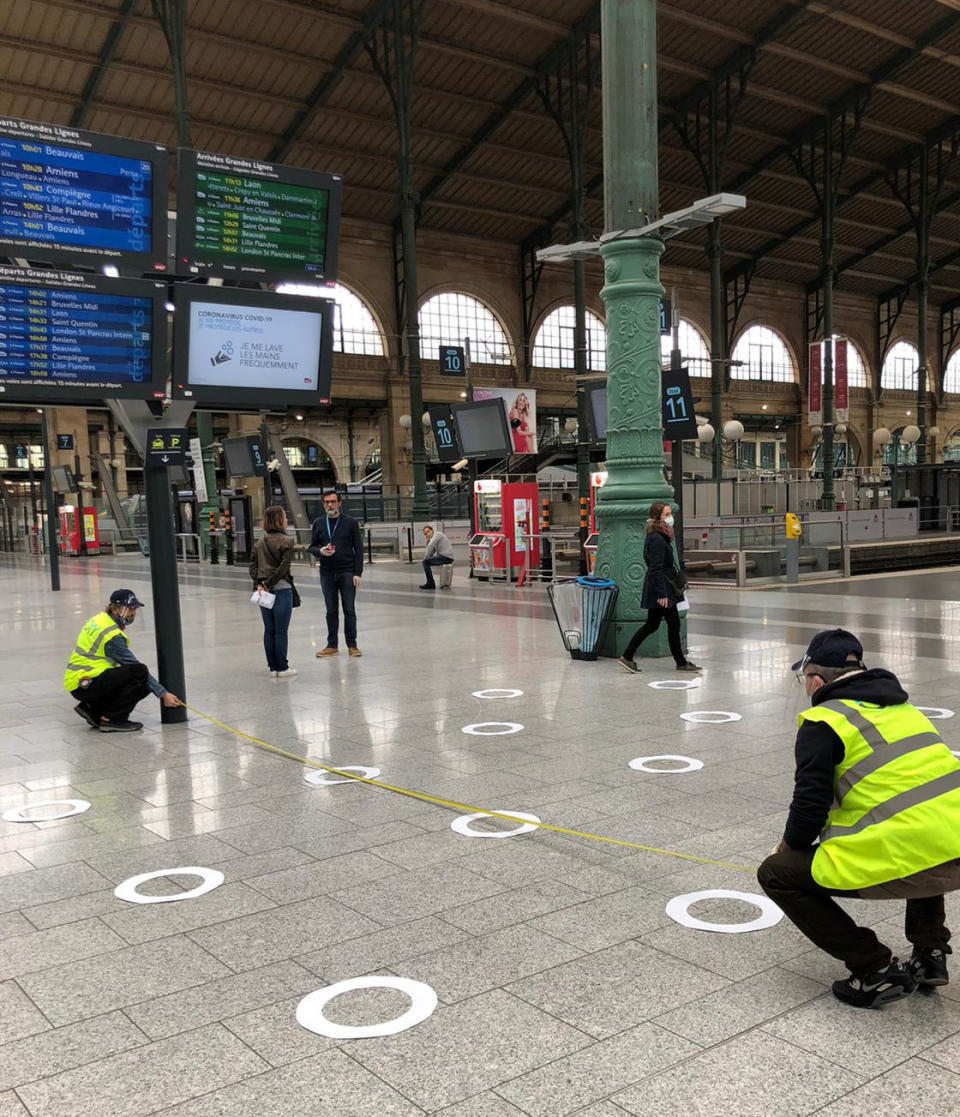 Frankreich, Paris: Arbeiter messen auf dem Boden gezeichnete Markierungen am Bahnhof Gare du Nord ab, die Passagiere in der Einhaltung eines Mindestabstands unterstützen sollen. Foto: Nicolas Garriga / AP / dpa