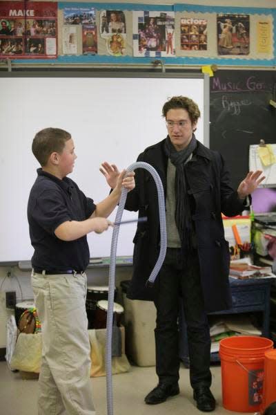 Teddy Abrams, music director of the Louisville Orchestra, works with an elementary school student to demonstrate how common objects like a vacuum cleaner hose can be used as a musical instrument.