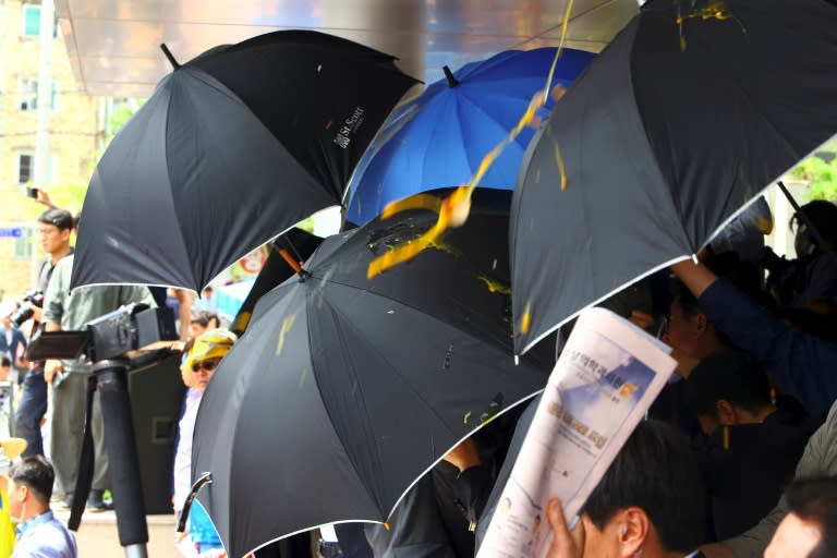 Officials use umbrellas to protect South Korean PM Hwang Kyo-Ahn from eggs and water bottles being thrown by angry protesters as he visits Seongju