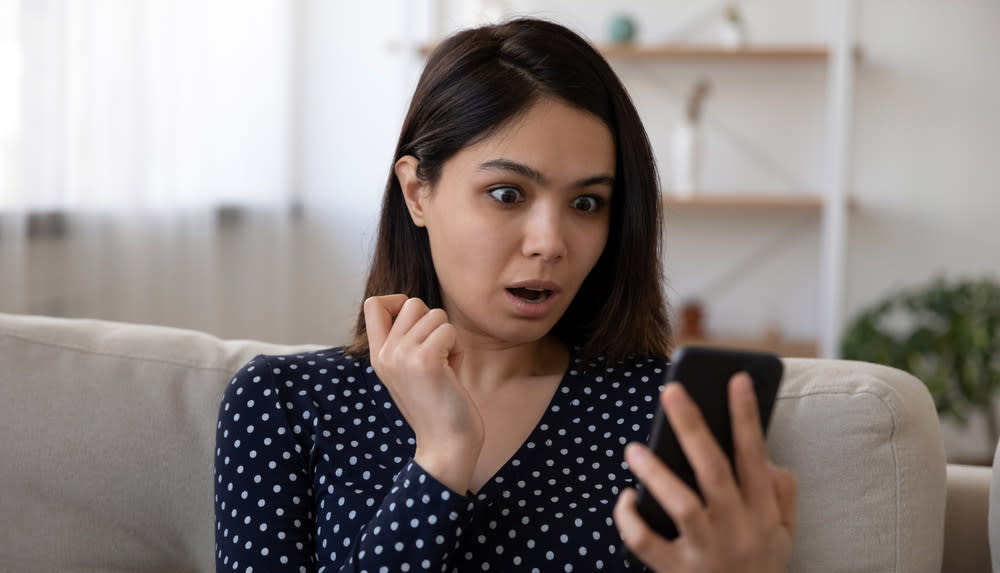  Dark-haired woman looking at smartphone screen in shock. 