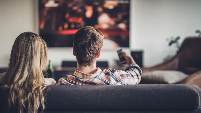 Back view of a couple watching TV on sofa in the living room.