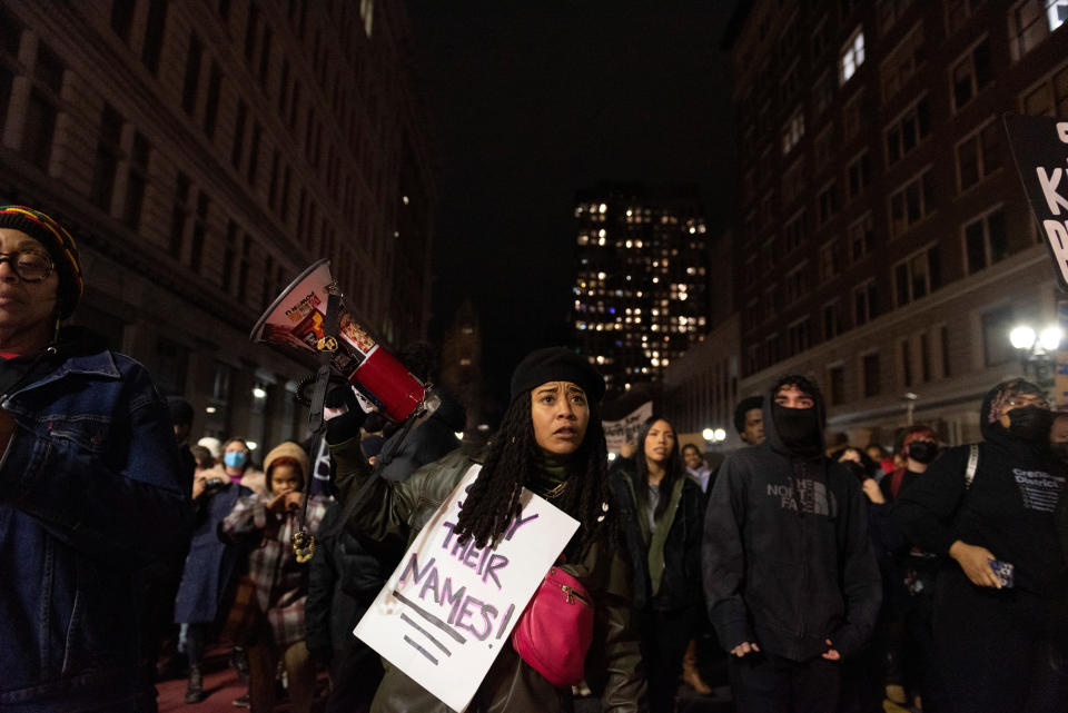 A woman holding a bullhorn during a protest in Oakland wears a sign that reads: Say their names.