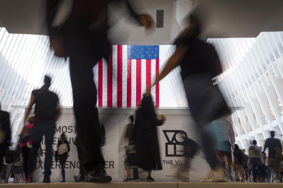 FILE - In this Sept. 11, 2019, file photo people walk past an American flag at the start of a work day, at the Oculus, part of the World Trade Center transportation hub in New York. On Friday, Oct. 4, the Commerce Department reports on the U.S. trade gap for August. (AP Photo/Wong Maye-E, File)