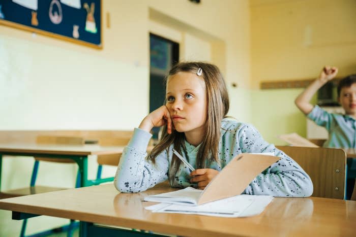 bored little girl sits at a school desk