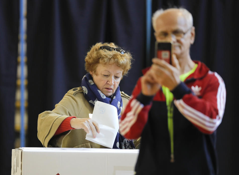 A man takes photos as a woman casts her vote in Bucharest, Romania, Sunday, Nov. 10, 2019. Voting got underway in Romania's presidential election after a lackluster campaign overshadowed by a political crisis which saw a minority government installed just a few days ago. (AP Photo/Vadim Ghirda)