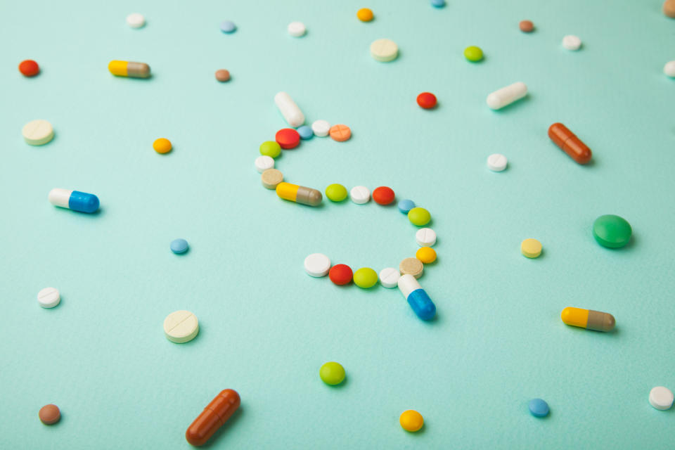 Pills of different colors scatter on a surface with some in the center arranged to form a dollar sign