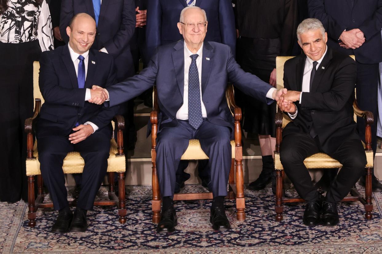 Israel's President Reuven Rivlin between Prime Minister Naftali Bennett and Foreign Minister Yair Lapid as they pose for a group photo with ministers of the new Israeli government (Reuters)