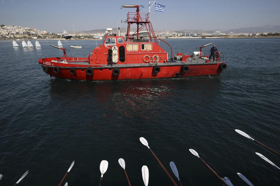 In this Sunday, Sept. 16, 2018 photo, a vessel of the Fire Department accompanies the Olympias, a replica of an ancient galley, at Saronic gulf in southern Athens. The 37-meter (121-foot) wooden vessel moored off southern Athens is an experimental reconstruction of the trireme, the sleek ancient Greek warship that halted a Persian invasion of Europe and ruled the Mediterranean for centuries. Every summer, visitors can get a whiff of life in the galleys 2,500 years ago by joining the crew of the Olympias _ and work up a sweat rowing it. (AP Photo/Thanassis Stavrakis)