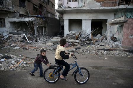 Children play on a bicycle near damaged buildings in the town of Douma, eastern Ghouta in Damascus November 5, 2015. REUTERS/Bassam Khabieh
