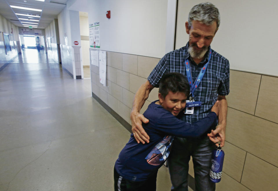 In this Sept. 19, 2019 photo, Gary Bass gets a hug in Santa Fe, new Mexico, from Jose Rodrigo Pena Ruiz, 10, a fifth grade student who wanted to know when he was going to Cambodia. The digital literacy teacher at El Camino Real Academy in Santa Fe is taking a one-month leave from his classroom to train English teachers in Kampot, Cambodia. (Luis Sanchez Saturno/Santa Fe New Mexican via AP)