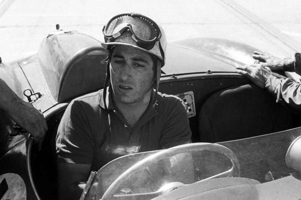 alfonso de portago wearing a helmet and sitting in his car as crew members prepare it