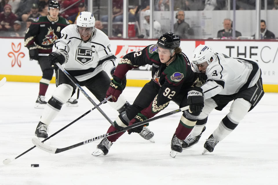 Arizona Coyotes center Logan Cooley (92) skates between Los Angeles Kings defenseman Matt Roy, right, and center Anze Kopitar (11) in the second period during an NHL hockey game, Friday, Oct. 27, 2023, in Tempe, Ariz. (AP Photo/Rick Scuteri)