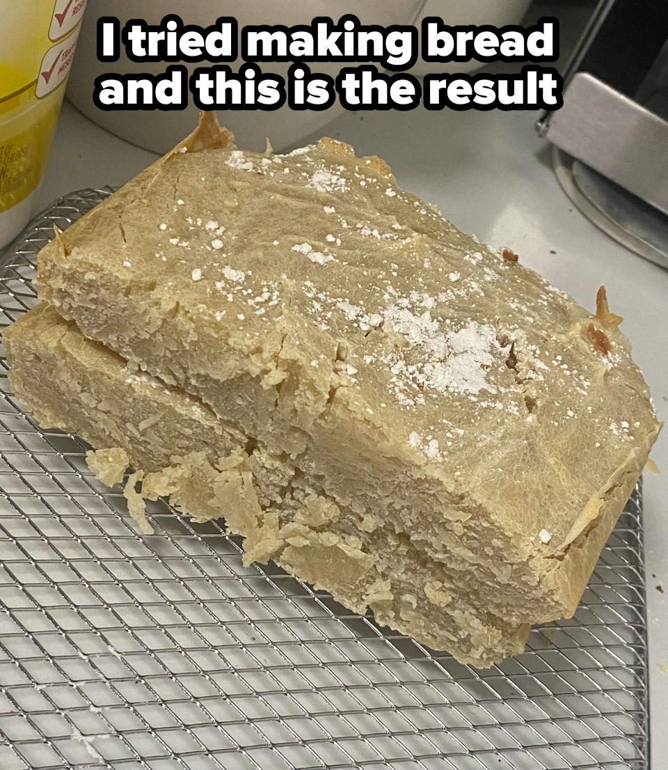 A vey dense loaf of bread with a thick, cracked crust, dusted with flour, on a wire cooling rack