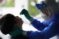 A clinic doctor collects sample for coronavirus testing from a man in Puchong, on the outskirt of Kuala Lumpur, Malaysia, Tuesday, Oct. 6, 2020. The health ministry has warned that Malaysia is facing a new wave of virus cases as the outbreak has widened in recent days. New clusters have sprung up in many states amid increased travel to eastern Sabah state, a hotspot zone, for a state election last month. (AP Photo/Vincent Thian)